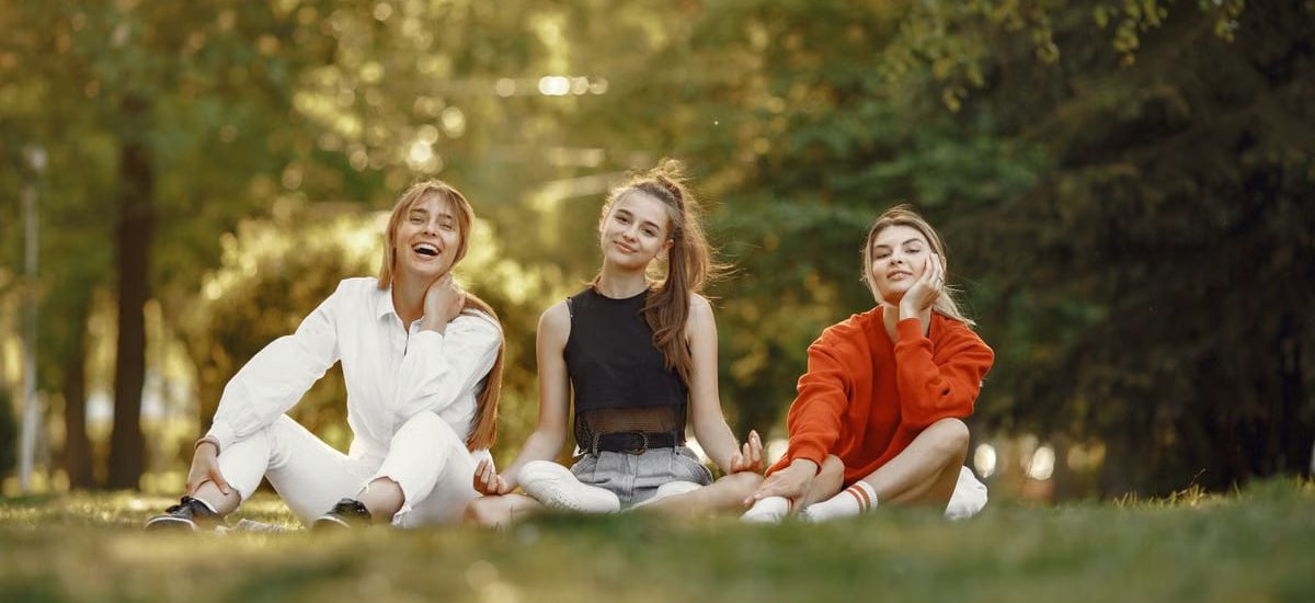 Three friends sitting on grass, enjoying a sunny outdoor day in the park.