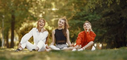 Three friends sitting on grass, enjoying a sunny outdoor day in the park.