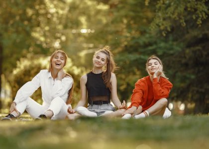 Three friends sitting on grass, enjoying a sunny outdoor day in the park.