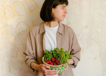 Woman standing with a basket of fresh greens and berries against a rustic wall background.