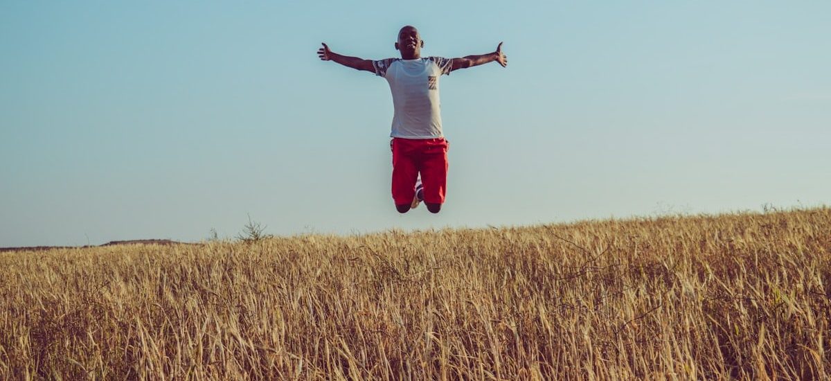 man in white shirt and red shorts jumping on brown grass field during daytime