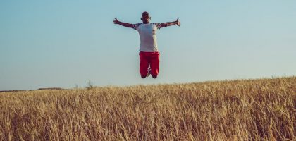man in white shirt and red shorts jumping on brown grass field during daytime