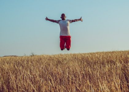 man in white shirt and red shorts jumping on brown grass field during daytime